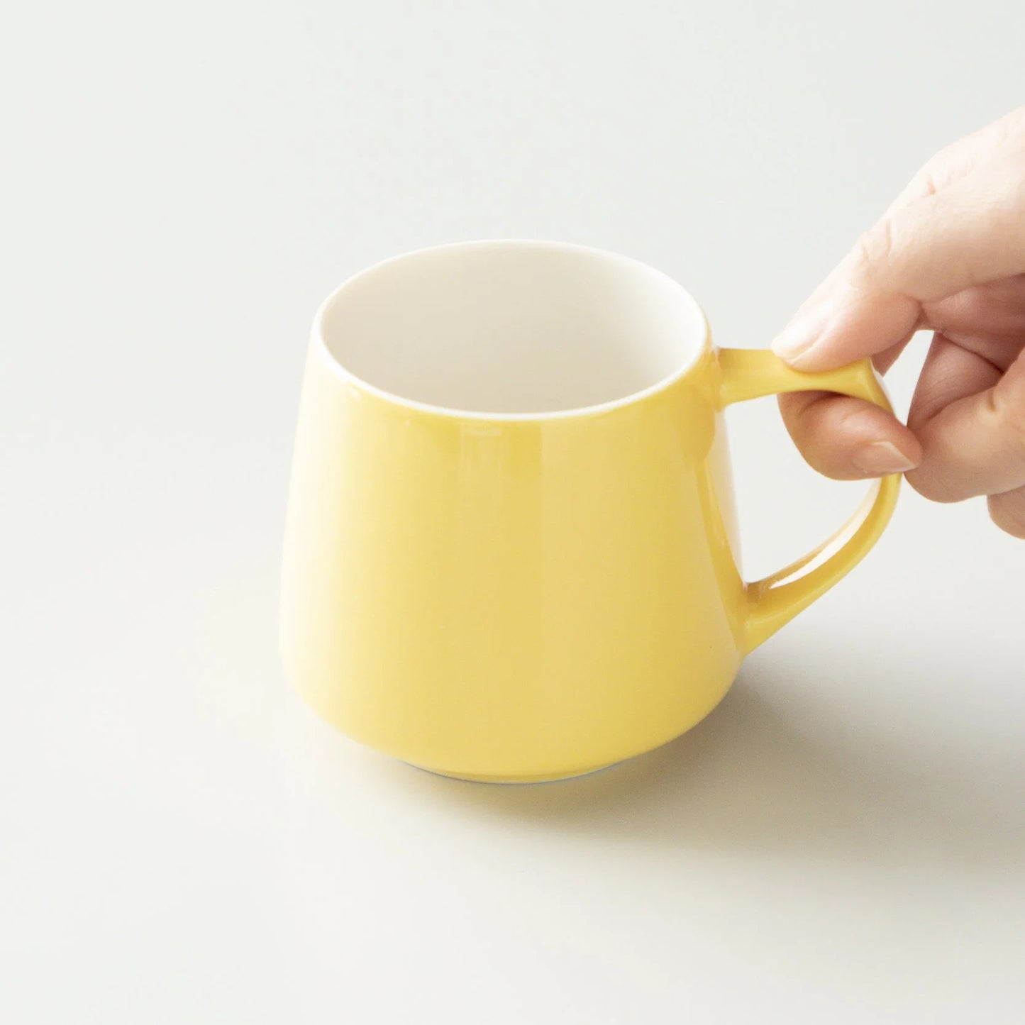 Yellow mug held by a hand on a light gray background #yellow