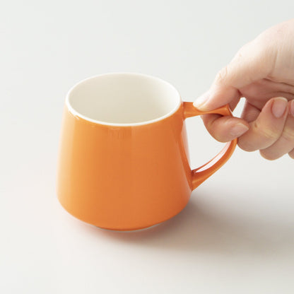 Orange mug with a hand holding its handle on a light gray background #orange